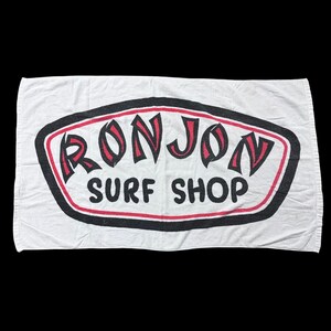 Op de afbeelding: Een witte keramische mok met een zwart handvat en de tekst "But First, Coffee" in een vetgedrukte, zwarte letter. De mok staat op een houten oppervlak. De mok is ongeveer 10 cm hoog.