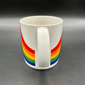 May include: White ceramic mug with a rainbow design. The rainbow is made up of red, orange, yellow, green, blue, and purple stripes.