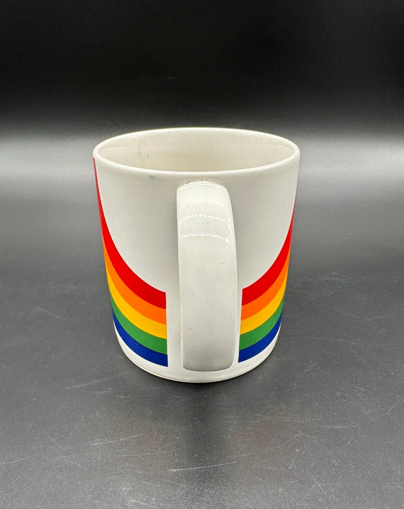 May include: White ceramic mug with a rainbow design. The rainbow is made up of red, orange, yellow, green, blue, and purple stripes.