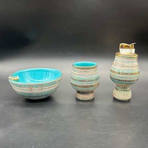 May include: A vintage ceramic ashtray, cup, and lighter set. The ashtray and cup have a turquoise interior and a textured exterior with blue, brown, and white stripes. The lighter has a gold-coloured top.