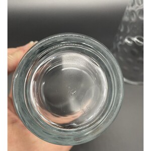 May include: Clear glass drinking glass with a textured surface. The bottom of the glass has the number "115" printed on it.