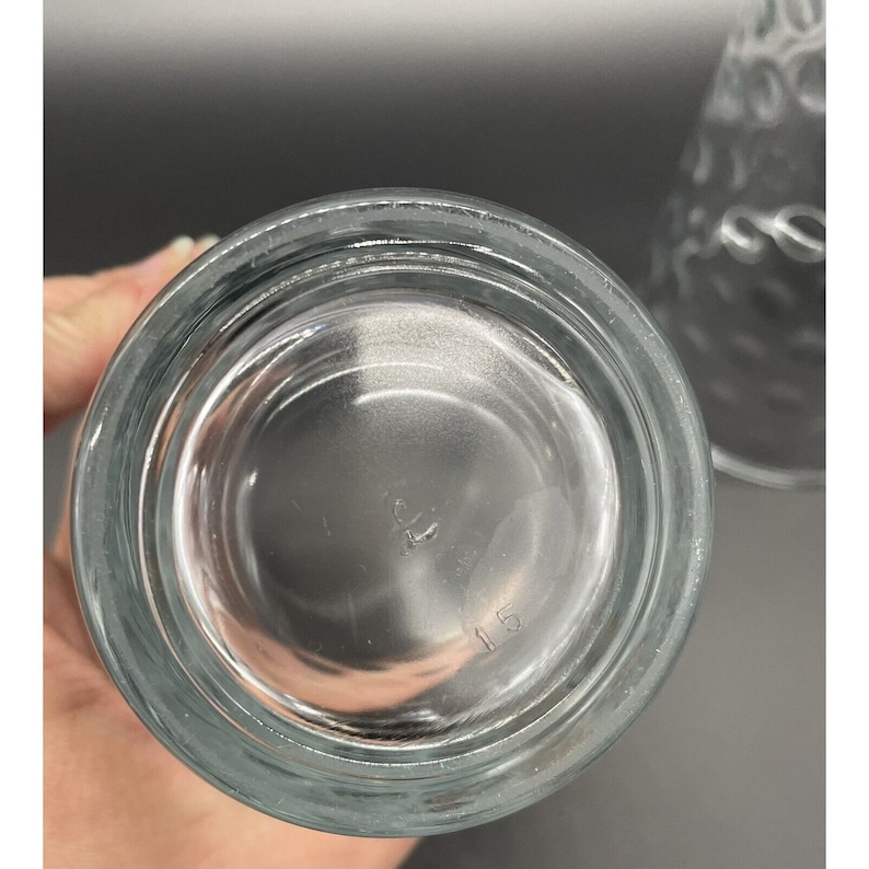 May include: Clear glass drinking glass with a textured surface. The bottom of the glass has the number "115" printed on it.