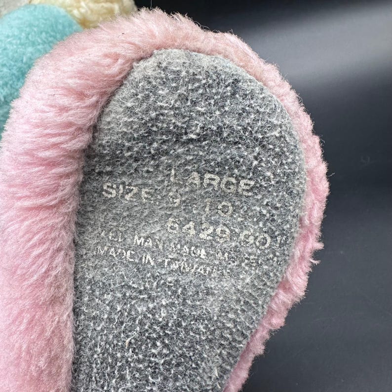Peut inclure: Gros plan d'une pantoufle rose et grise. La pantoufle a une bordure rose duveteuse et une semelle grise. La semelle est marqu&eacute;e "LARGE" et "MADE IN TAIWAN". La pantoufle est une taille 9.