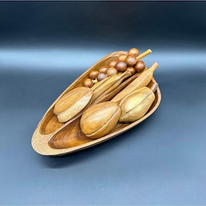 May include: A wooden fruit bowl with a carved design. The bowl is filled with wooden fruit, including grapes, bananas, and pears.