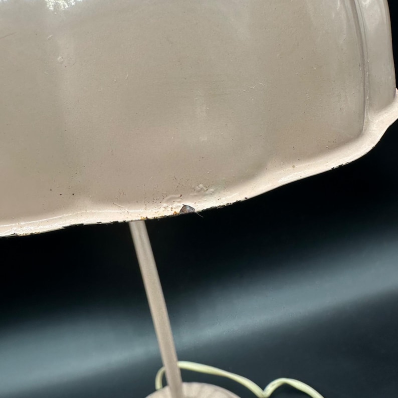 K&ouml;nnte beinhalten: Nahaufnahme einer cremefarbenen Vintage-Tischlampe. Die Lampe hat einen abgerundeten Schirm und einen schlanken, gebogenen Stiel. Der Schirm hat ein leicht abgenutztes Aussehen mit kleinen Unvollkommenheiten. Die Lampe steht vor einem dunklen Hintergrund.
