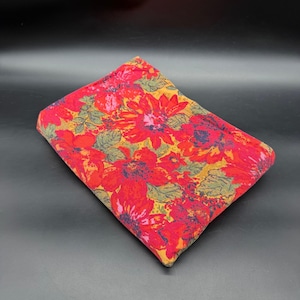 May include: A rectangular fabric piece featuring a vibrant floral pattern with large red and orange flowers, dark blue accents, and green leaves set against a golden yellow background. The textile is folded into a compact, flat, rectangular shape.