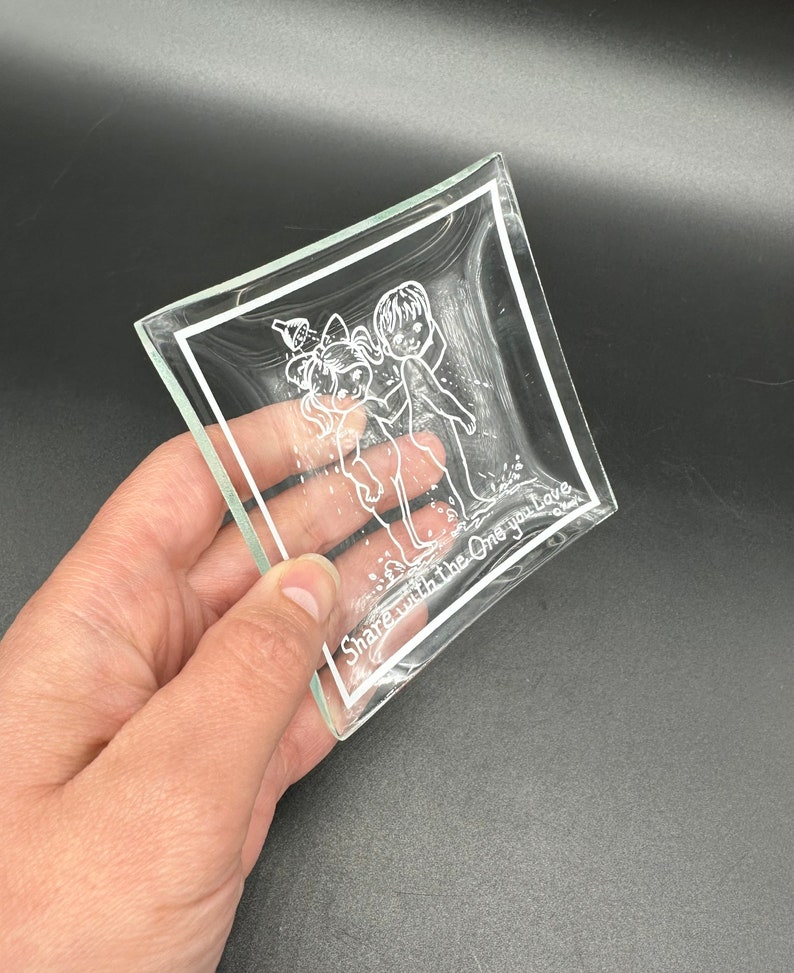 May include: A clear glass trinket dish with a white etched design of two children holding hands. The text "Share with the One you Love" is etched on the bottom of the dish.
