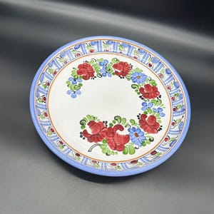 May include: A white ceramic plate with a blue and white border and a floral design painted in red, blue, and green.
