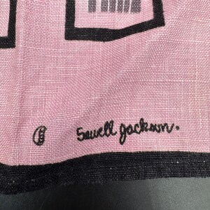 Pu&ograve; includere: Primo piano di un tessuto rosa con forme geometriche nere e un bordo nero. Il testo "Sawell Jackson" &egrave; ricamato in corsivo nero. Il tessuto ha una trama.