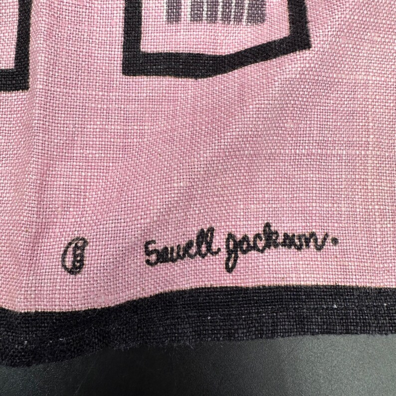 Pu&ograve; includere: Primo piano di un tessuto rosa con forme geometriche nere e un bordo nero. Il testo "Sawell Jackson" &egrave; ricamato in corsivo nero. Il tessuto ha una trama.