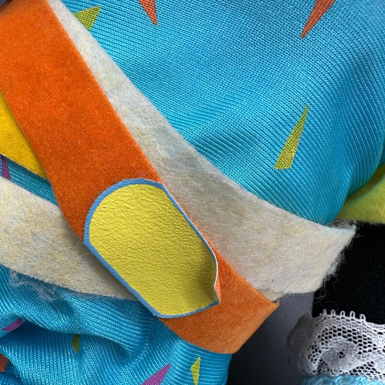 Peut inclure: Gros plan sur un tissu bleu et orange avec un patch jaune. Le tissu pr&eacute;sente un motif g&eacute;om&eacute;trique de triangles de diff&eacute;rentes couleurs.