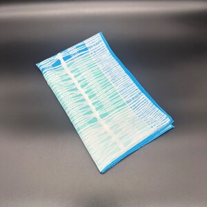 May include: A white and blue patterned fabric scarf with a blue border. The pattern is a series of vertical lines with a gradient of blue.