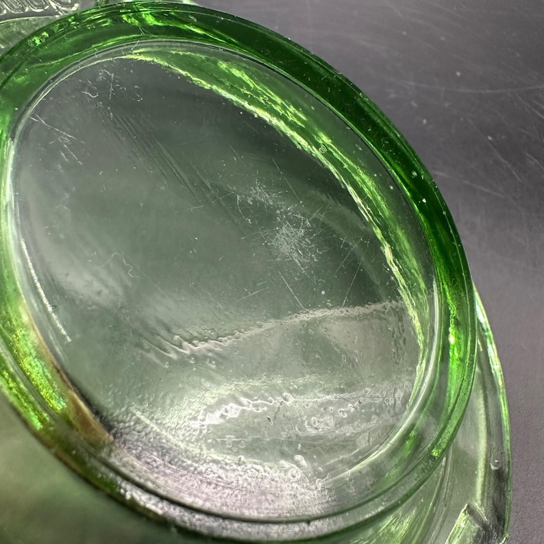 May include: Close-up of a green glass dish with an oval shape. The glass has a slight tint and visible scratches on the surface. The rim of the dish is thicker and more vibrant in color.
