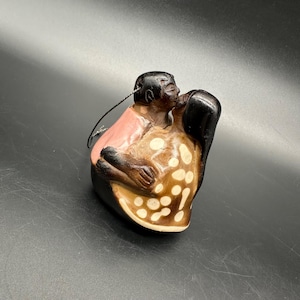 Puede incluir: Una figurita de cerámica de una pareja besándose, pintada en marrón, rosa y blanco. La mujer lleva un vestido de lunares marrones y blancos y el hombre lleva una camisa rosa.