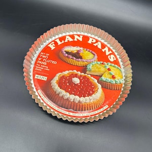 May include: A set of two vintage flan pans with a red and gold design. The packaging features illustrations of decorated flans and text that reads "FLAN PANS" and "9" Fluted Pans" (approx. 23 cm). The pans are for baking sponge cake shells.