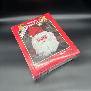 Peut inclure: Kit de loisirs créatifs WonderArt Noël représentant une tête de Père Noël avec un chapeau rouge et une barbe blanche. Le kit est facile à réaliser en 2 heures et comprend 17 oz de matériaux. Art. #K131.