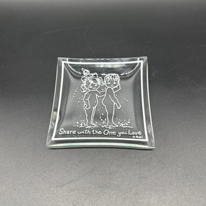 May include: A clear glass dish with a raised design of two children holding a watering can. The dish has a white border and the text "Share with the One you Love" at the bottom.