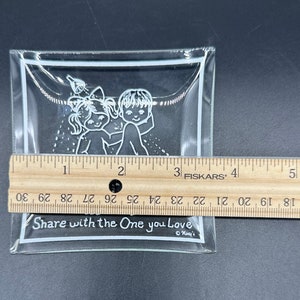 May include: A clear glass dish with a white outline and a design of two children holding hands. The dish has the text "Share with the One you Love" printed on the bottom.