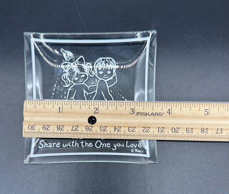 May include: A clear glass dish with a white outline and a design of two children holding hands. The dish has the text "Share with the One you Love" printed on the bottom.