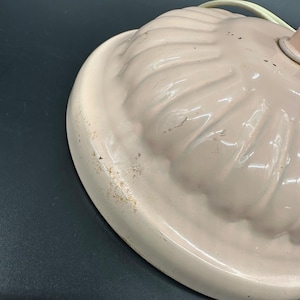 K&ouml;nnte beinhalten: Nahaufnahme eines Vintage-Lampenfu&szlig;es mit hellrosa, gewelltem Rand. Der Sockel hat ein strukturiertes, geriffeltes Design und einen wei&szlig;en Rand. Der Lampenfu&szlig; weist Gebrauchsspuren mit Verf&auml;rbungen und Kratzern auf.