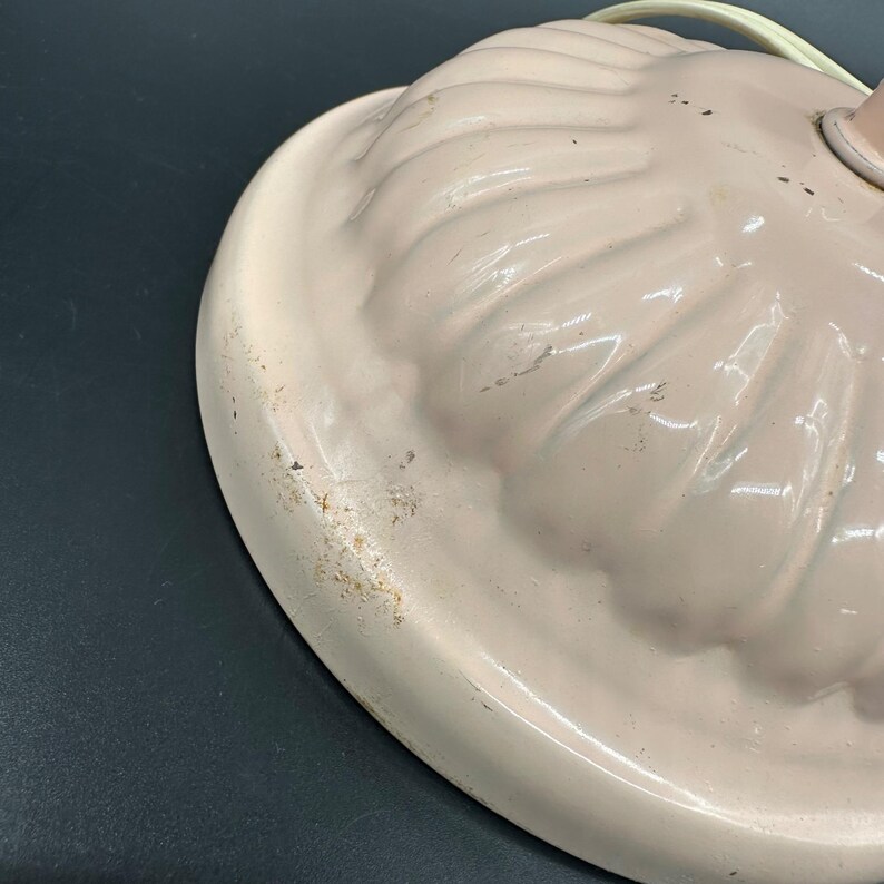 K&ouml;nnte beinhalten: Nahaufnahme eines Vintage-Lampenfu&szlig;es mit hellrosa, gewelltem Rand. Der Sockel hat ein strukturiertes, geriffeltes Design und einen wei&szlig;en Rand. Der Lampenfu&szlig; weist Gebrauchsspuren mit Verf&auml;rbungen und Kratzern auf.