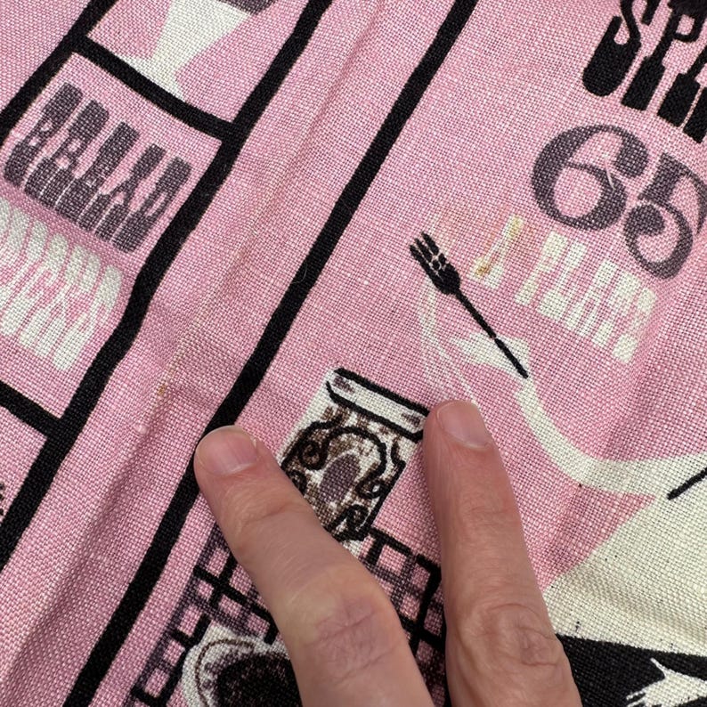 Pu&ograve; includere: Tessuto rosa con un motivo a griglia nera e illustrazioni a tema cibo. Il tessuto presenta la parola "BREAD" e il numero "65". Sono visibili anche una forchetta e un barattolo.