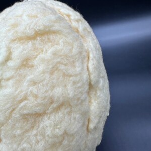 Peut inclure: Gros plan sur un objet cr&egrave;me, duveteux et textur&eacute;. Le mat&eacute;riau semble doux et dense, avec une surface l&eacute;g&egrave;rement irr&eacute;guli&egrave;re. Le fond est d'une couleur sombre et unie, contrastant avec l'objet clair.