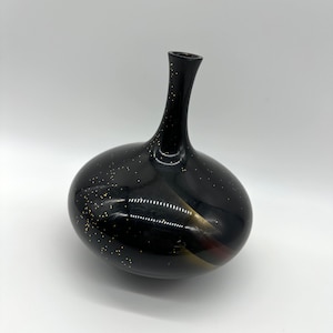 May include: A black ceramic vase with gold and red accents. The vase has a round body and a long, thin neck.