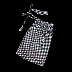 Könnte beinhalten: Eine schwarz-weiße Gingham-Schürze mit rotem und weißem Besatz. Die Schürze hat einen Halteband am Hals und ein langes Band, das sich um die Taille wickelt.