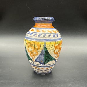Puede incluir: Un jarrón de cerámica pintado a mano con cuerpo redondeado y cuello estrecho. El jarrón presenta un diseño vibrante con colores naranja, amarillo, azul y verde. El diseño incluye formas geométricas y patrones florales. El jarrón mide unos 15 cm de alto.