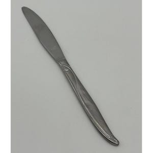 May include: A stainless steel butter knife with a decorative handle. The knife has a smooth, curved blade and a handle with a stylized floral design. The handle also features small starburst patterns.
