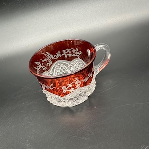 Könnte beinhalten: Eine klare Glas Tasse mit rotem Boden und einem weißen, geätzten Design. Das Design beinhaltet ein Blumenmuster und die Worte "Angel of the Morning".