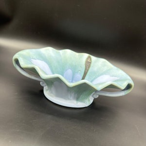 May include: A blue and green ceramic bowl with two handles. The bowl has a wavy rim and a unique glaze.