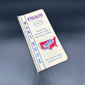 以下が含まれることがあります： 上部にCraigのロゴが入った、ヴィンテージの螺旋綴じ「Want Book」。表紙にはテキストとNifdaのロゴ、シェフのいるミズーリ州の赤いアウトラインが特徴です。本はクリーム色で、青色のアクセントと金属製のスパイラルバインディングが施されています。