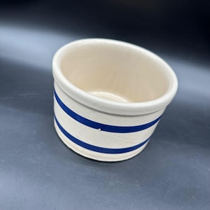 Puede incluir: Olla de cerámica color crema con dos rayas azules horizontales. El pequeño recipiente redondo tiene un borde ligeramente inclinado y un acabado liso y brillante. Un artículo de cocina clásico de estilo vintage.