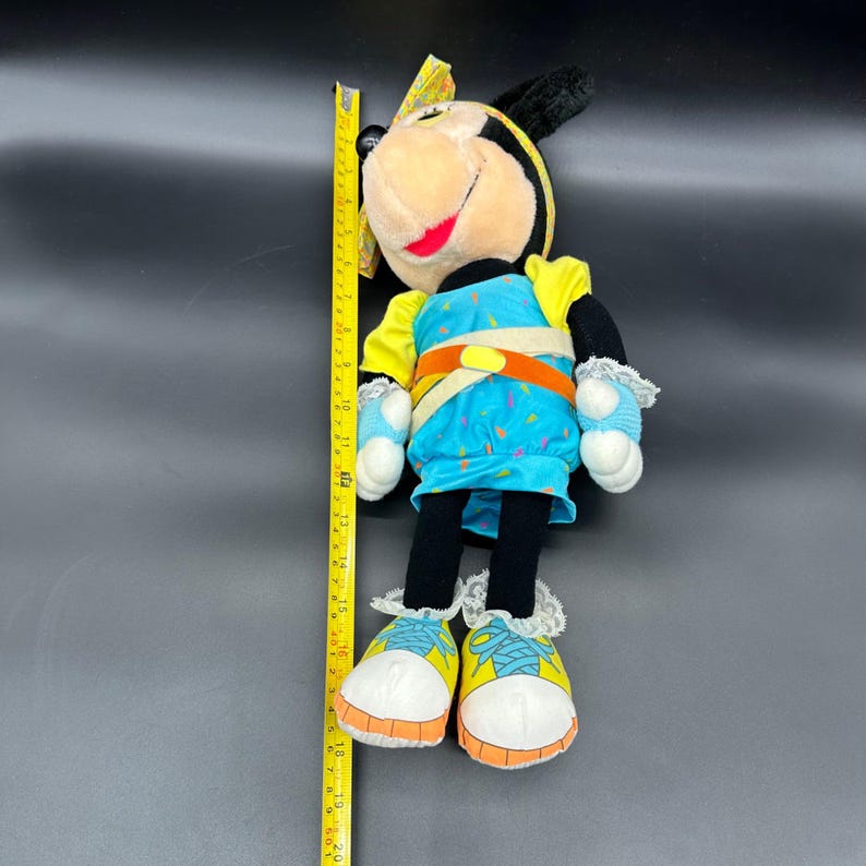 Peut inclure: Une poup&eacute;e en peluche vintage de Minnie Mouse portant une tenue bleue et jaune avec un n&oelig;ud blanc. La poup&eacute;e mesure environ 46 cm de haut et a un nez et des yeux noirs.