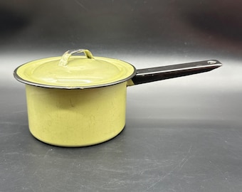 May include: A vintage, light yellow saucepan with a lid and a black handle. The pot has a black rim and a matching handle. The lid has a small handle for easy lifting. The saucepan is likely made of enamel or a similar material.