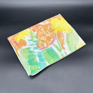 May include: Folded white fabric with a colorful floral pattern. The design features large yellow, orange, and green watercolor-style flowers and leaves. The fabric is folded neatly, showcasing the vibrant print against a dark background.
