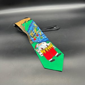 May include: A green, blue, and brown Christmas tie with a cartoon image of Santa Claus holding a string of fish and reindeer in the background.