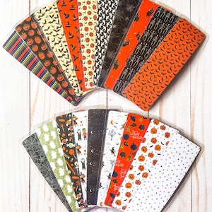 May include: A set of 18 Halloween-themed bookmarks featuring various designs, including bats, pumpkins, ghosts, and candy corn. The bookmarks are printed on white cardstock and have a clear plastic coating.