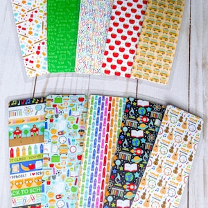 May include: A set of ten colorful bookmarks featuring various school-themed patterns. The patterns include school buses, apples, crayons, musical instruments, and a schoolhouse. The bookmarks are all in a clear plastic sleeve.