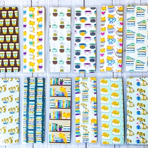 May include: A collection of colorful bookmarks with various patterns. Designs include coffee cups, cats with coffee, teacups, stacks of books, dogs with books, and dogs with coffee. Each bookmark is rectangular and encased in clear plastic.