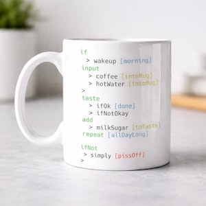 May include: White ceramic mug with a large handle. The mug features a humorous programming-style text in green, including "wakeup," "coffee," and "pissOff." The mug is designed for coffee or tea and is suitable for home or office use.