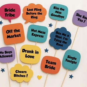 May include: A collection of colorful photo booth props on wooden sticks. The props feature phrases like "Bride Tribe," "Last Fling Before the Ring," and "Off the Market." Star and heart-shaped confetti are scattered around the props, perfect for a bachelorette party.