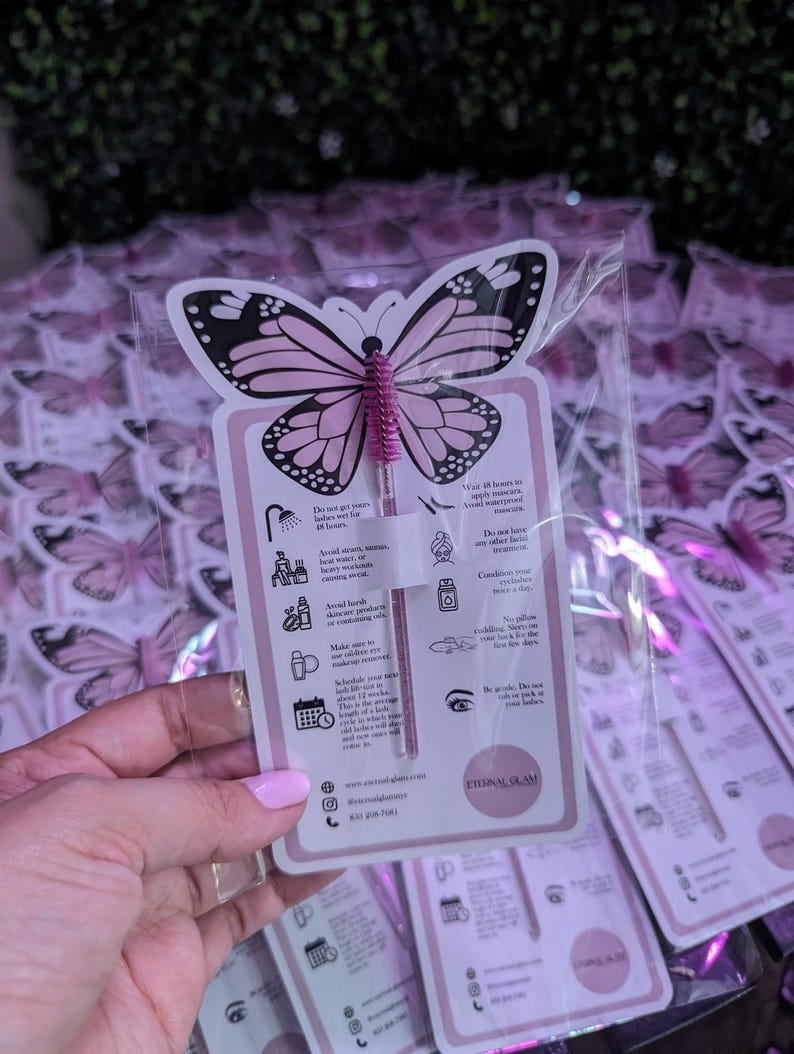 K&ouml;nnte beinhalten: Eine rosa und schwarz geformte Karte in Schmetterlingsform mit einer rosa Mascarab&uuml;rste. Die Karte enth&auml;lt Anweisungen und den Text "Eternal Glam". Der Hintergrund zeigt mehrere &auml;hnliche Karten in Klarsichtverpackungen.