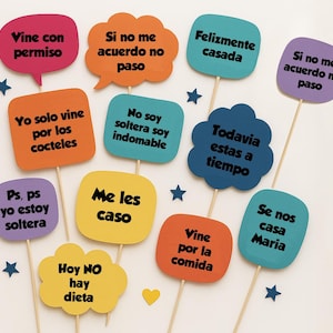 May include: A collection of colorful speech bubble photo booth props on wooden sticks. Each prop has a different phrase in Spanish, such as "I only came for the cocktails" and "I'm still single."
