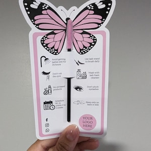 Può includere: Una scheda a forma di farfalla rosa e nera con un design a spazzola per mascara. La scheda include istruzioni per la cura delle ciglia, come evitare di bagnare le ciglia e usare un applicatore per ciglia. La scheda ha uno spazio per un logo.