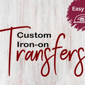 May include: Custom Iron-on Transfers text in a burgundy script font, with the word "Transfers" in a larger font size. The text is on a white wood grain background. A burgundy circle with the words "Easy DIY" and an iron graphic is in the upper right corner.