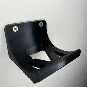 Peut inclure: Support mural en plastique noir avec deux trous de vis et un design incurv&eacute;. Le support a une forme d&eacute;coup&eacute;e pour maintenir un objet.