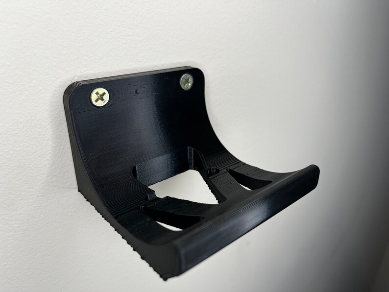 Peut inclure: Support mural en plastique noir avec deux trous de vis et un design incurv&eacute;. Le support a une forme d&eacute;coup&eacute;e pour maintenir un objet.